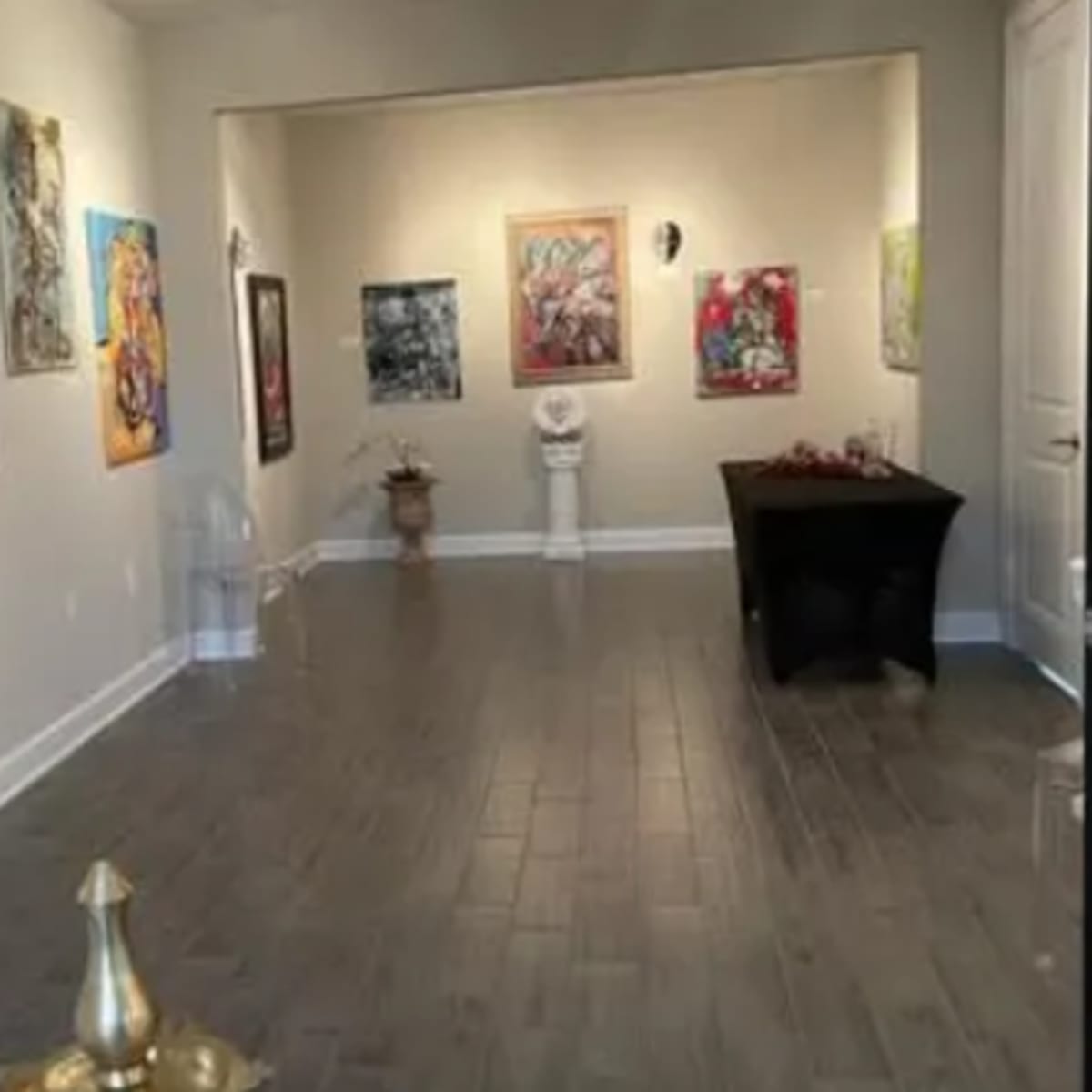 An art gallery with colorful paintings displayed on the walls and a table in the center of the room.