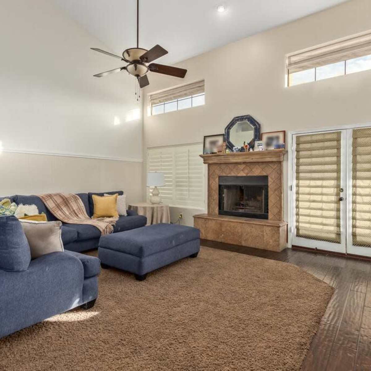 The living room features a blue sectional sofa, a matching ottoman, a fireplace with a stone surround, and large windows allowing natural light to enter.