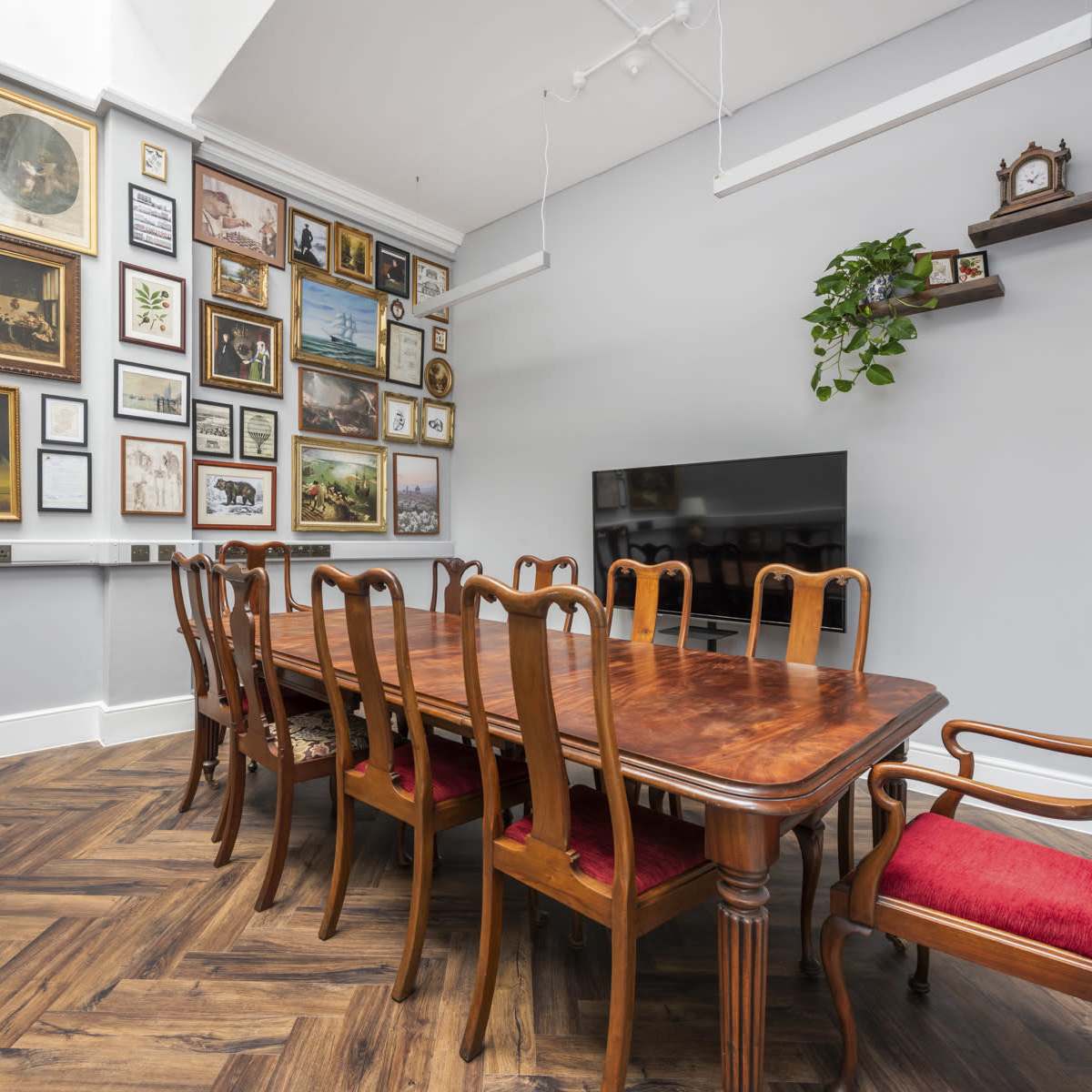 A dining room features a long wooden table surrounded by chairs, with a wall displaying an array of framed artwork and photographs.