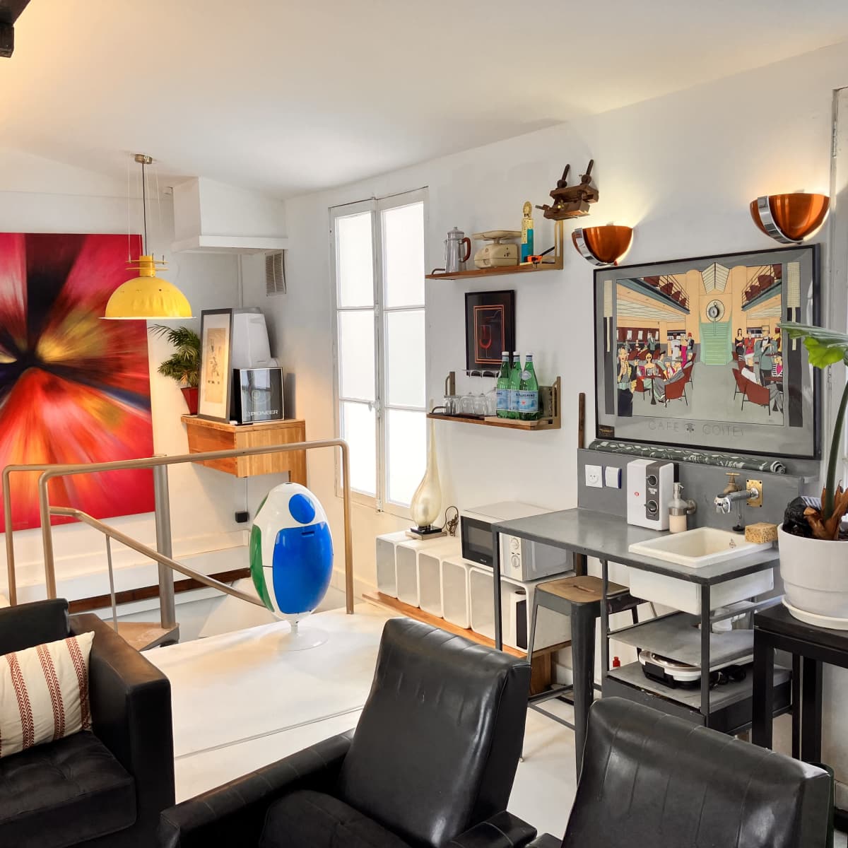 A modern living space with colorful artwork, a yellow pendant light, and a stylish seating area featuring black chairs and a decorative plant.