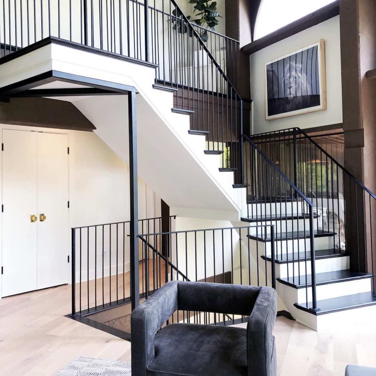 A modern interior with a staircase featuring black railings, a large window, and a seating area with a dark armchair.