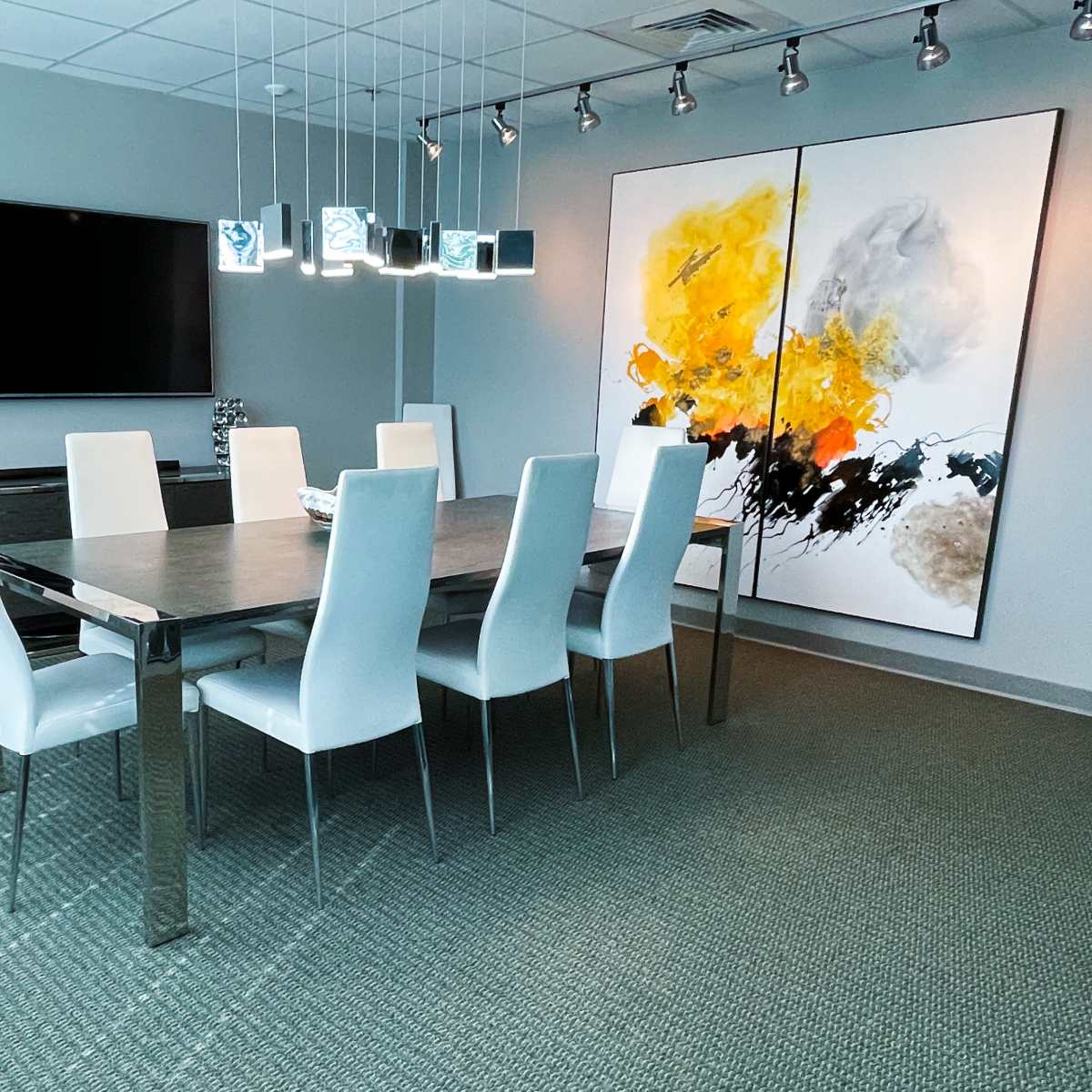 A modern conference room with a long table surrounded by white chairs, a large artwork on the wall, and a television mounted above a side cabinet.