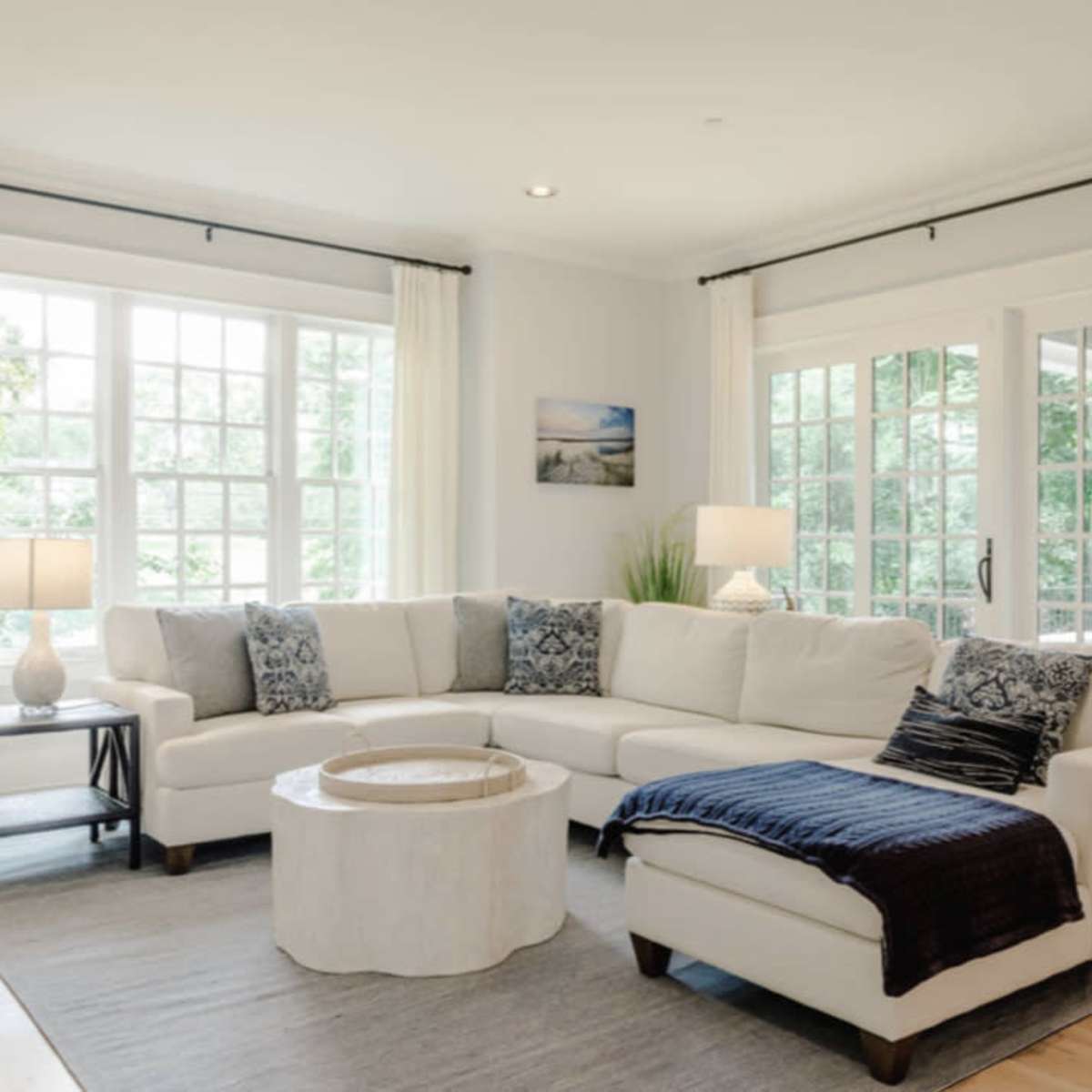 A bright living room featuring a large white sectional sofa, a circular coffee table, and large windows with natural light.