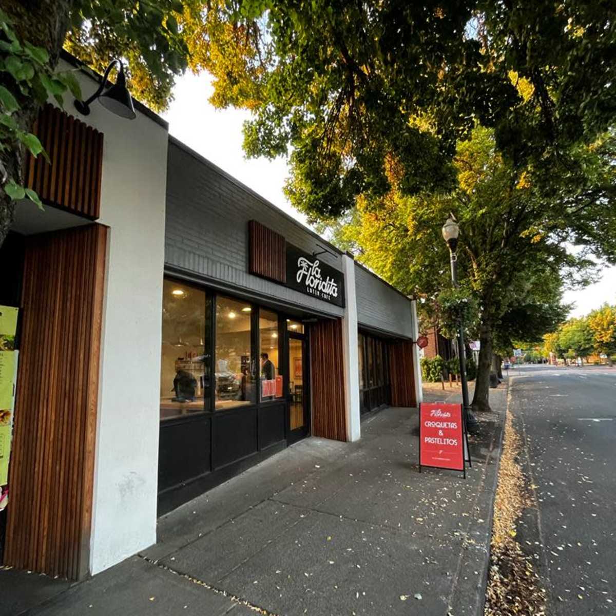 A storefront with a sign that reads "The Horditis," located on a sidewalk lined with trees.
