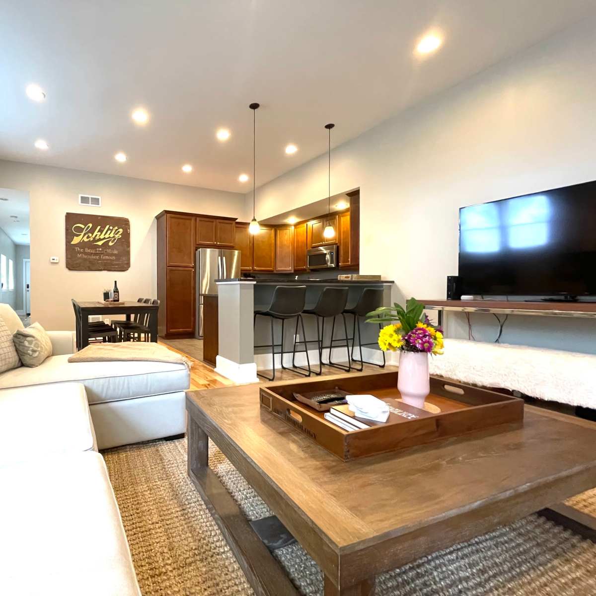 A modern living room with a sectional sofa, a wooden coffee table, a dining area, and a kitchen in the background.