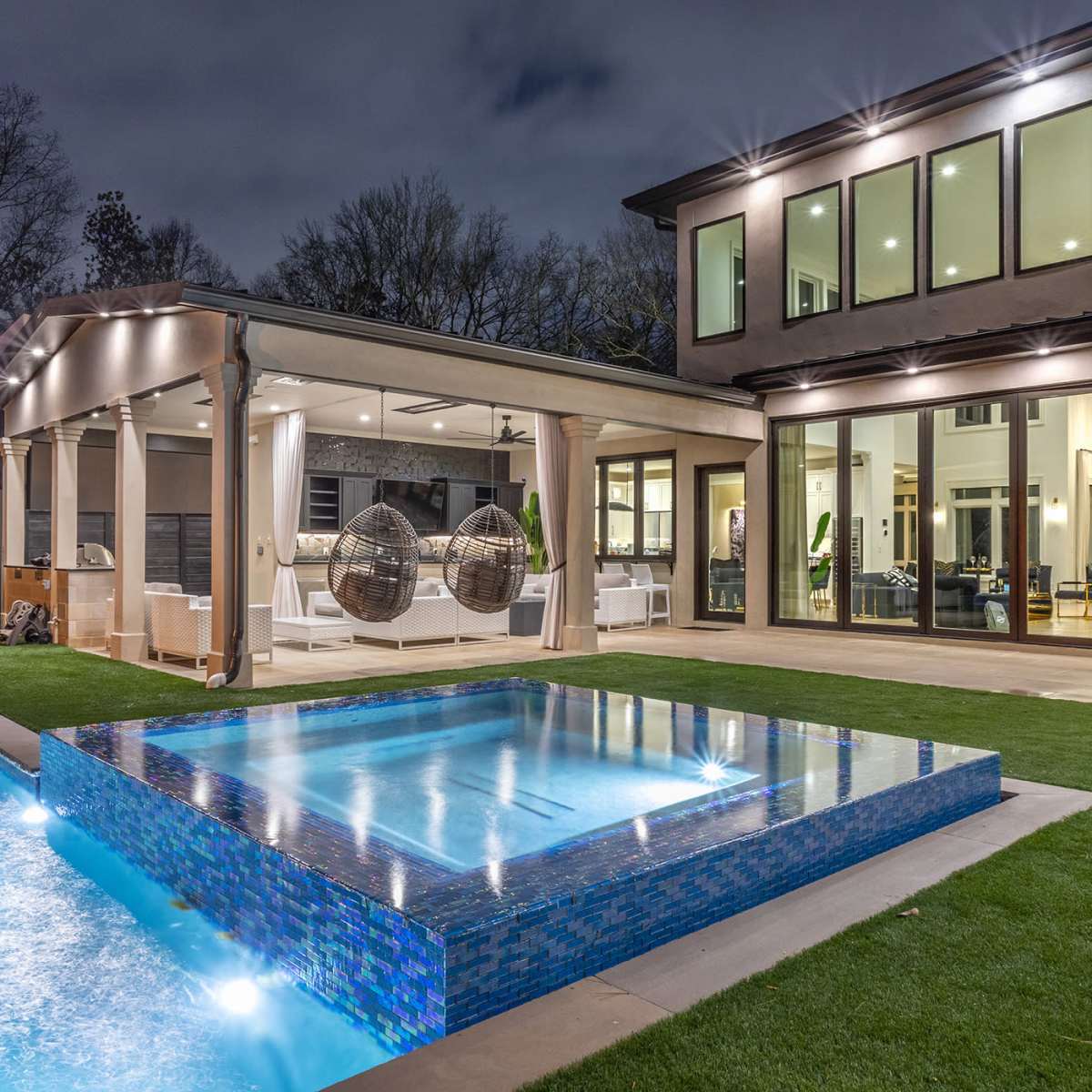 A modern backyard featuring a swimming pool and a spa, with a covered patio and large windows on the house.