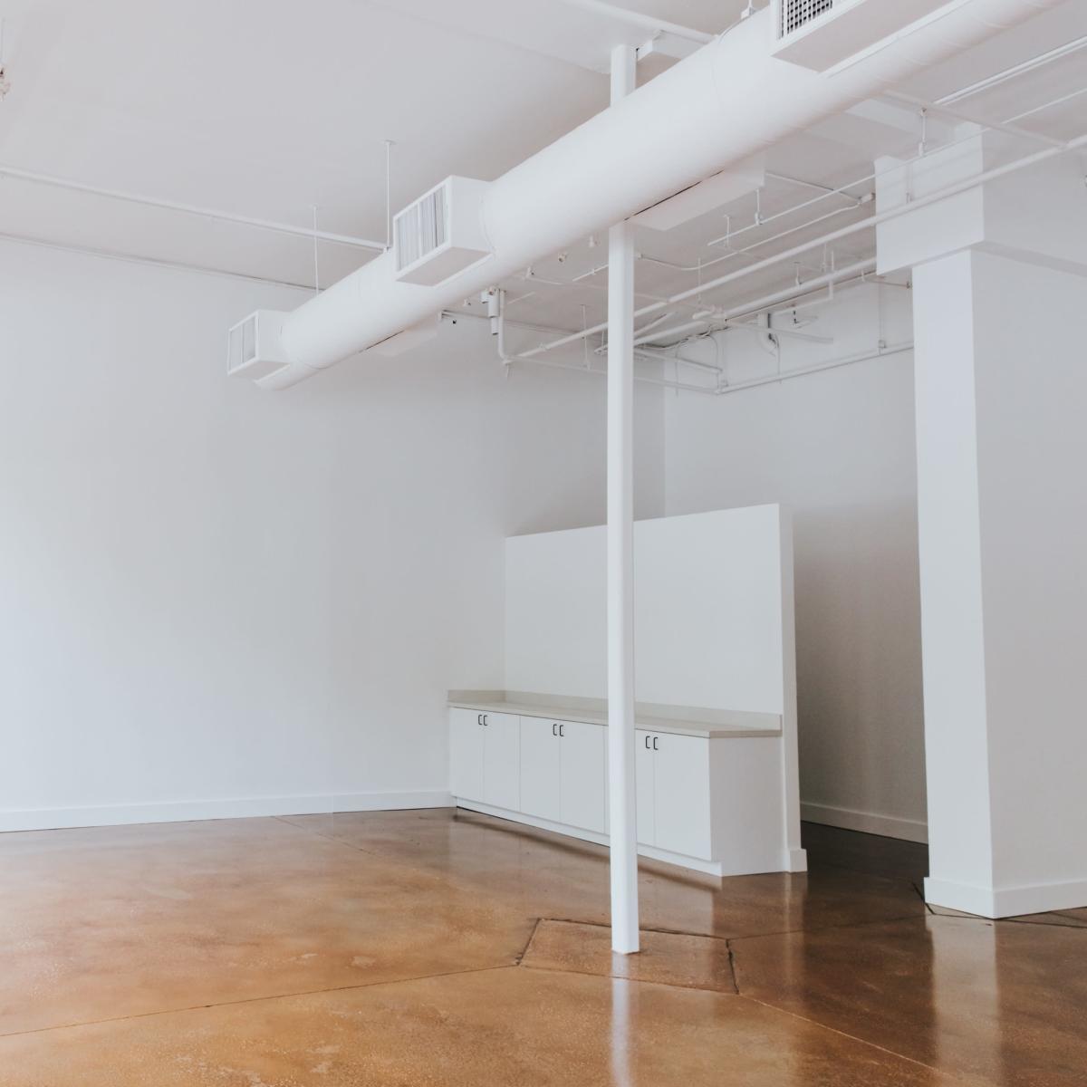 An empty, modern room with large windows, bare walls, and a small cabinet along one side.