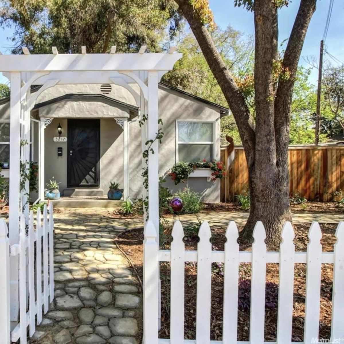 A small, gray house with a white picket fence and a stone pathway leading to the front door.