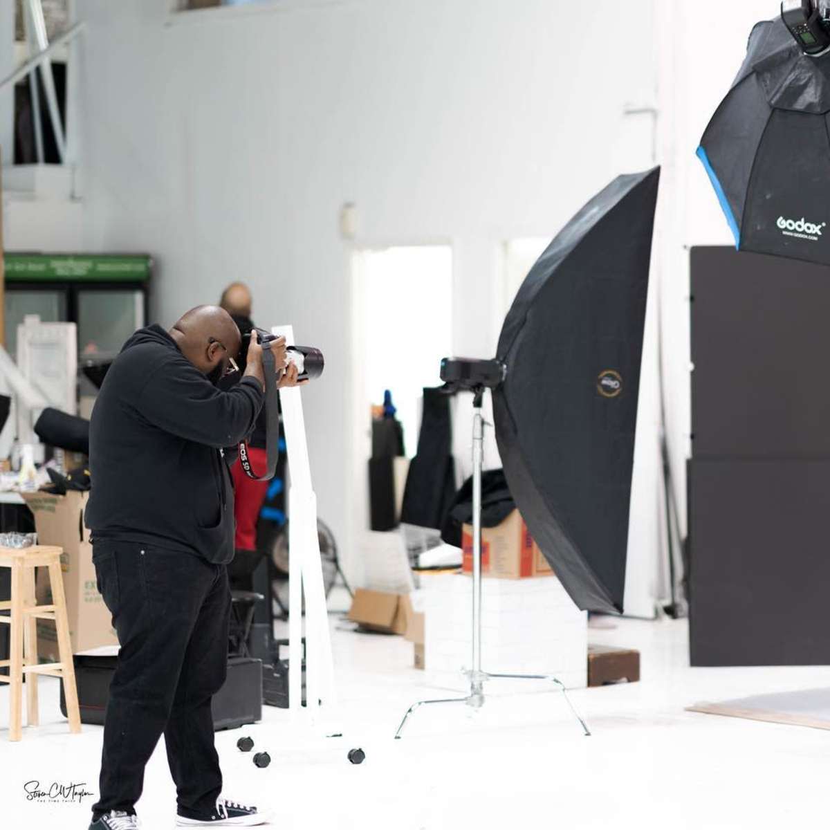A photographer captures a model in a studio equipped with various lighting setups and backdrops.