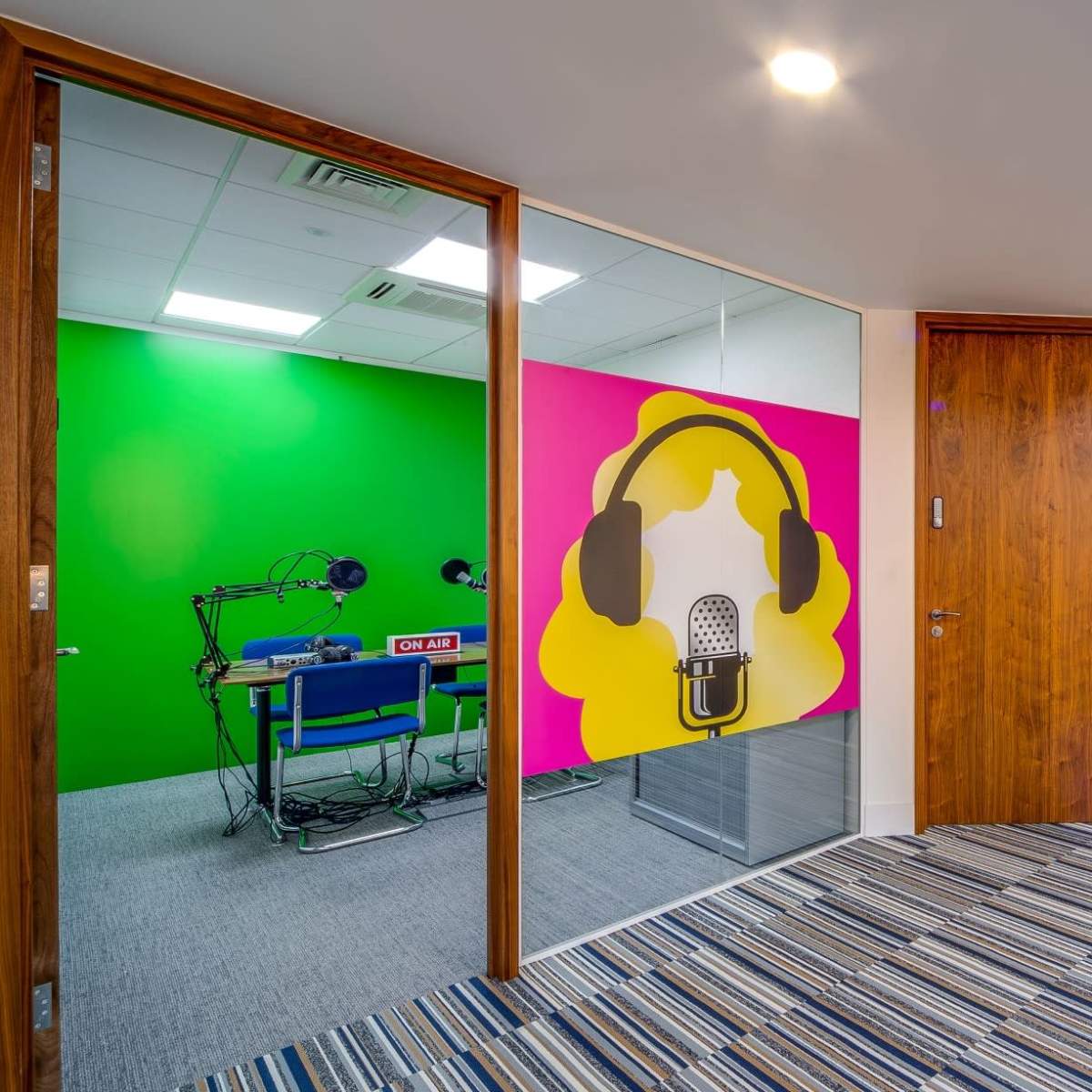 A hallway with two glass-doored rooms, one featuring a green wall with a microphone design and headphones, and the other displaying a purple wall covered in words like "OPPORTUNITY" and "EXCELLENCE."