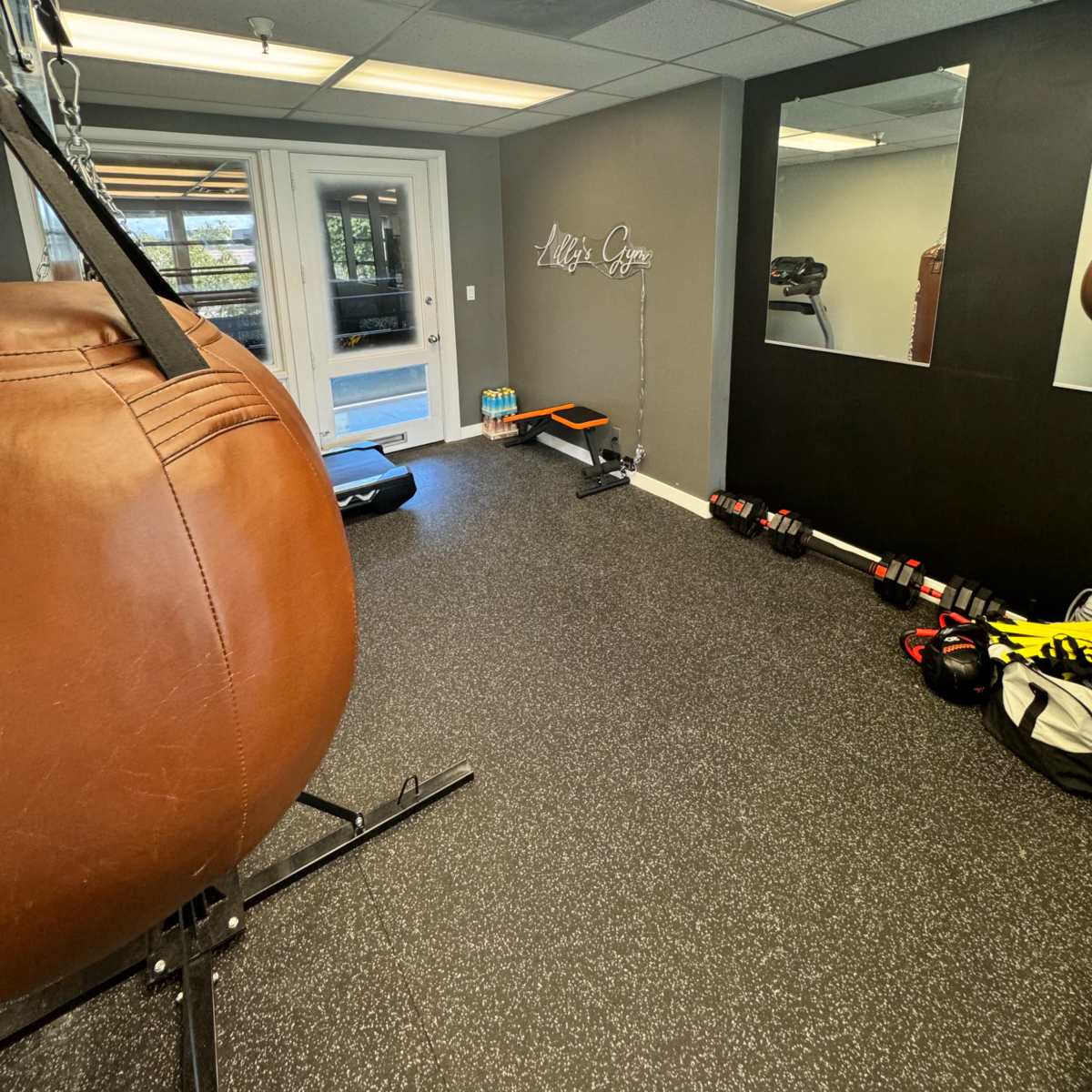 A sparsely furnished gym with a heavy bag, dumbbells, and a mirror on one wall.