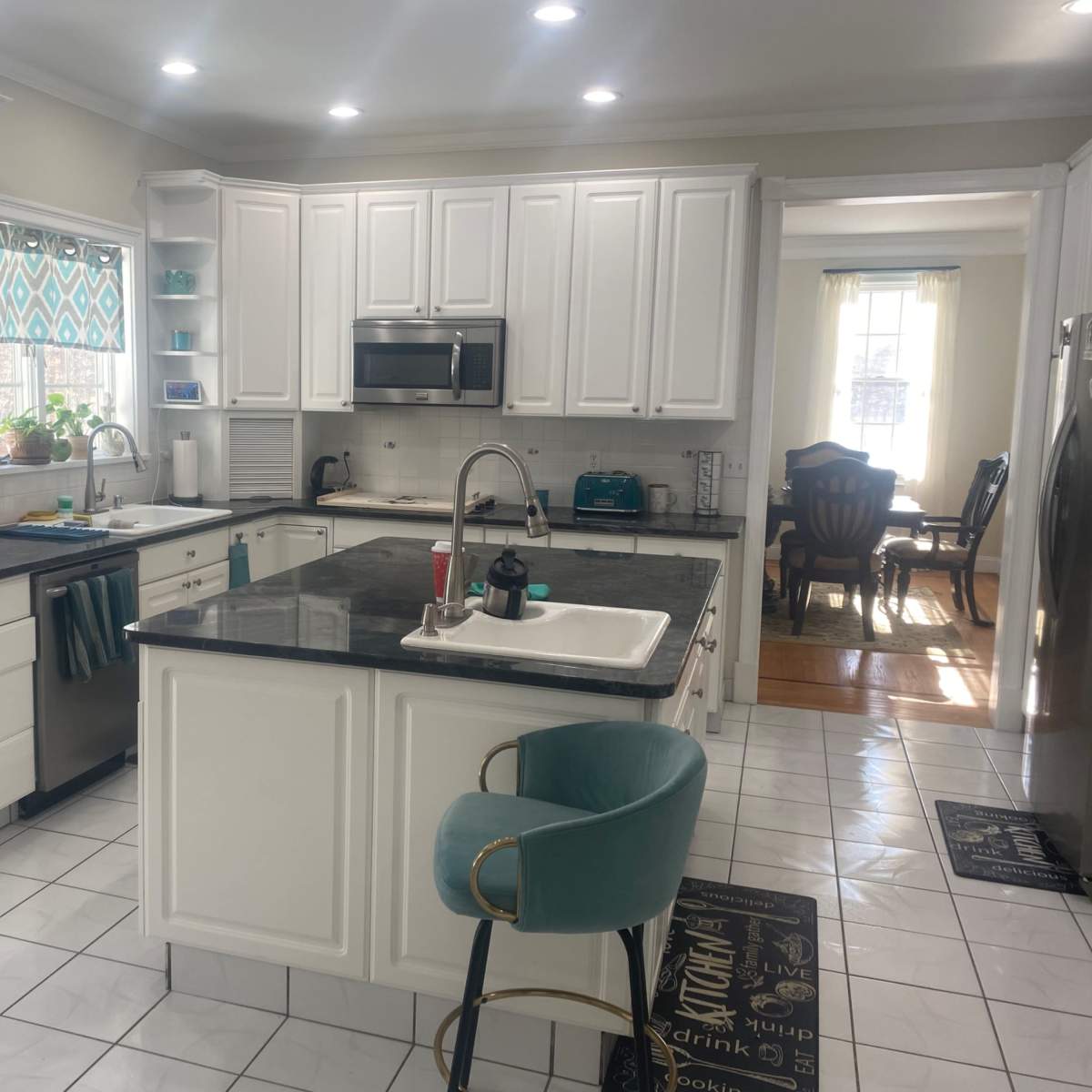 A modern kitchen with white cabinetry, a black countertop, and a dining area visible through an open layout.