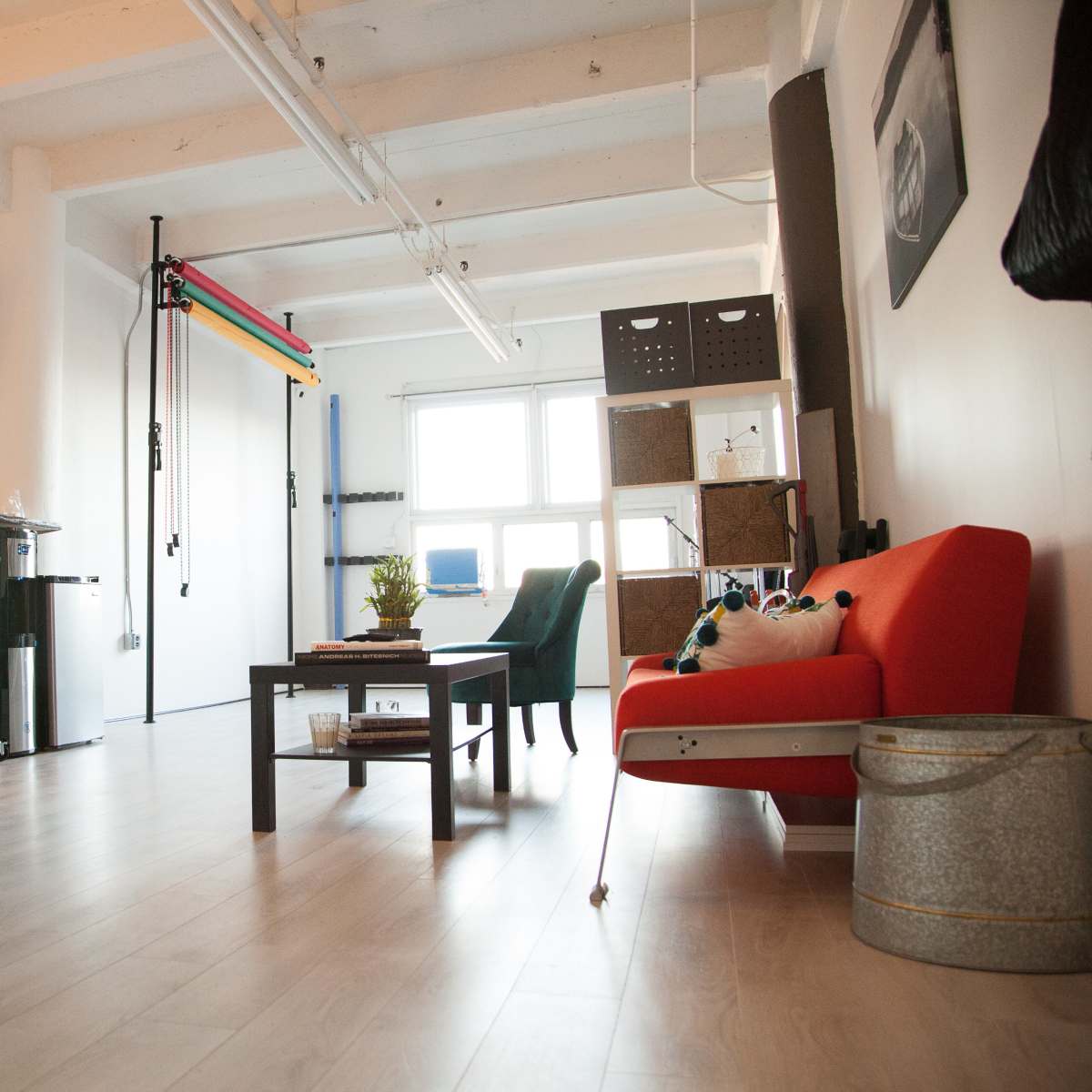A modern, minimalistic living space featuring a red sofa, a coffee table, a small dining area, and a workspace with a TV mounted on the wall.