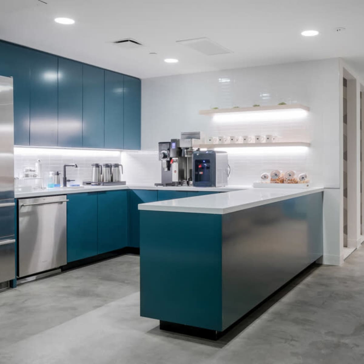 A modern kitchen with teal cabinetry, stainless steel appliances, and a white countertop.