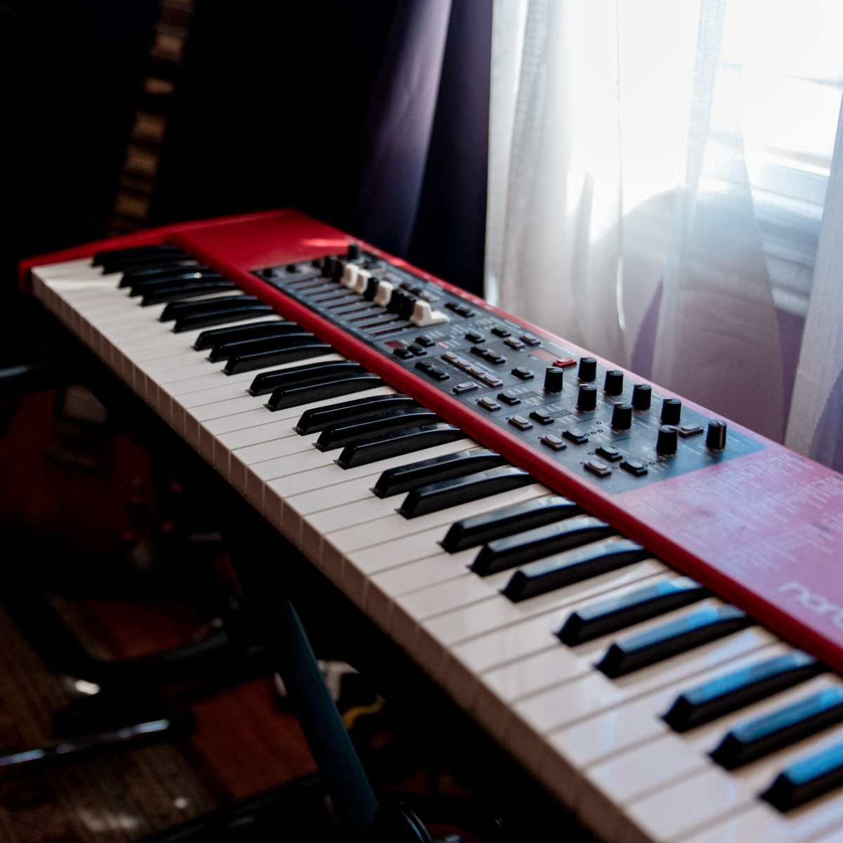 A red keyboard with black and white keys sits near a window, illuminated by natural light.
