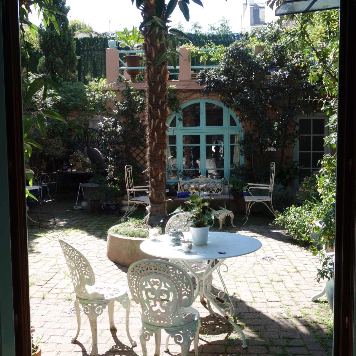 A well-maintained courtyard features a round table and chairs surrounded by greenery and various plants.