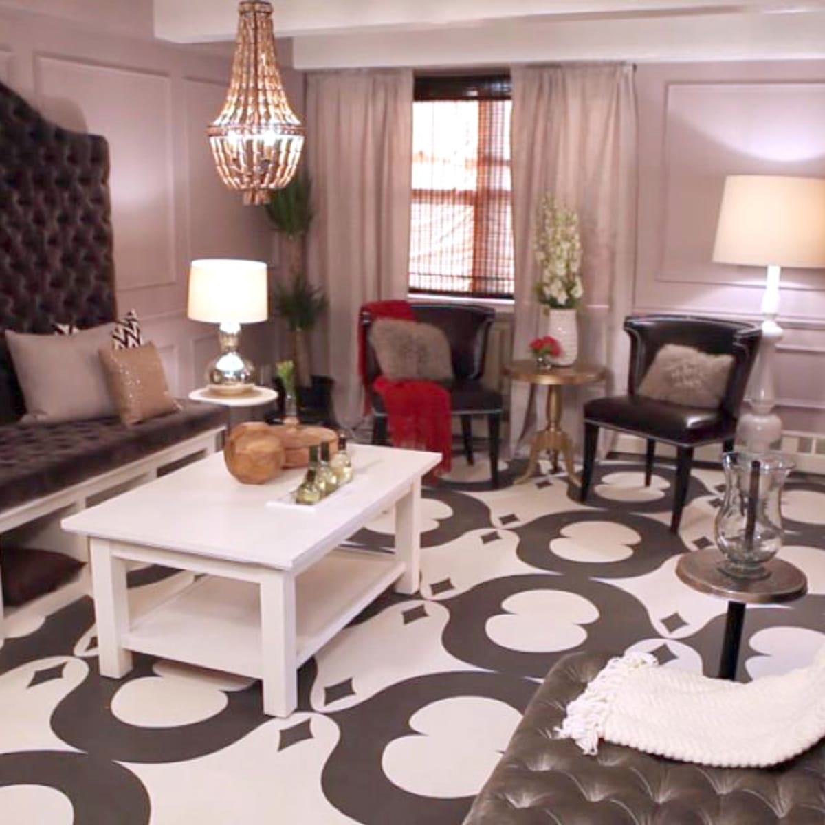 The living room features a tufted dark sofa, a coffee table, and a patterned floor with a chandelier hanging above.