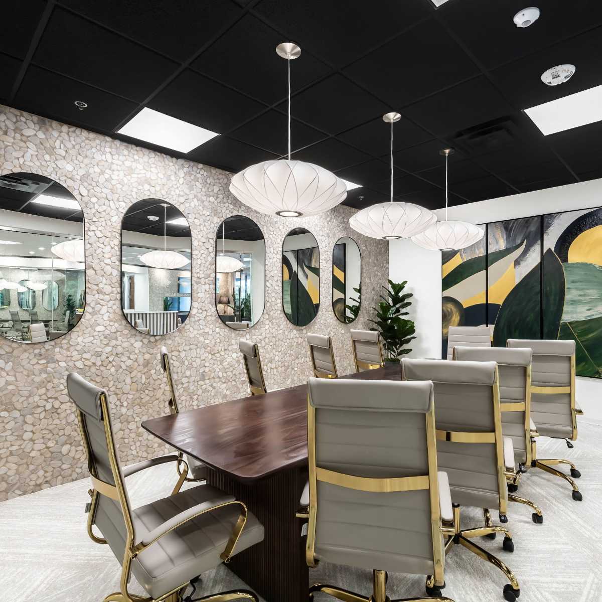 A modern conference room features a long wooden table surrounded by gray leather chairs, with a textured stone wall and several round mirrors, illuminated by pendant lights.