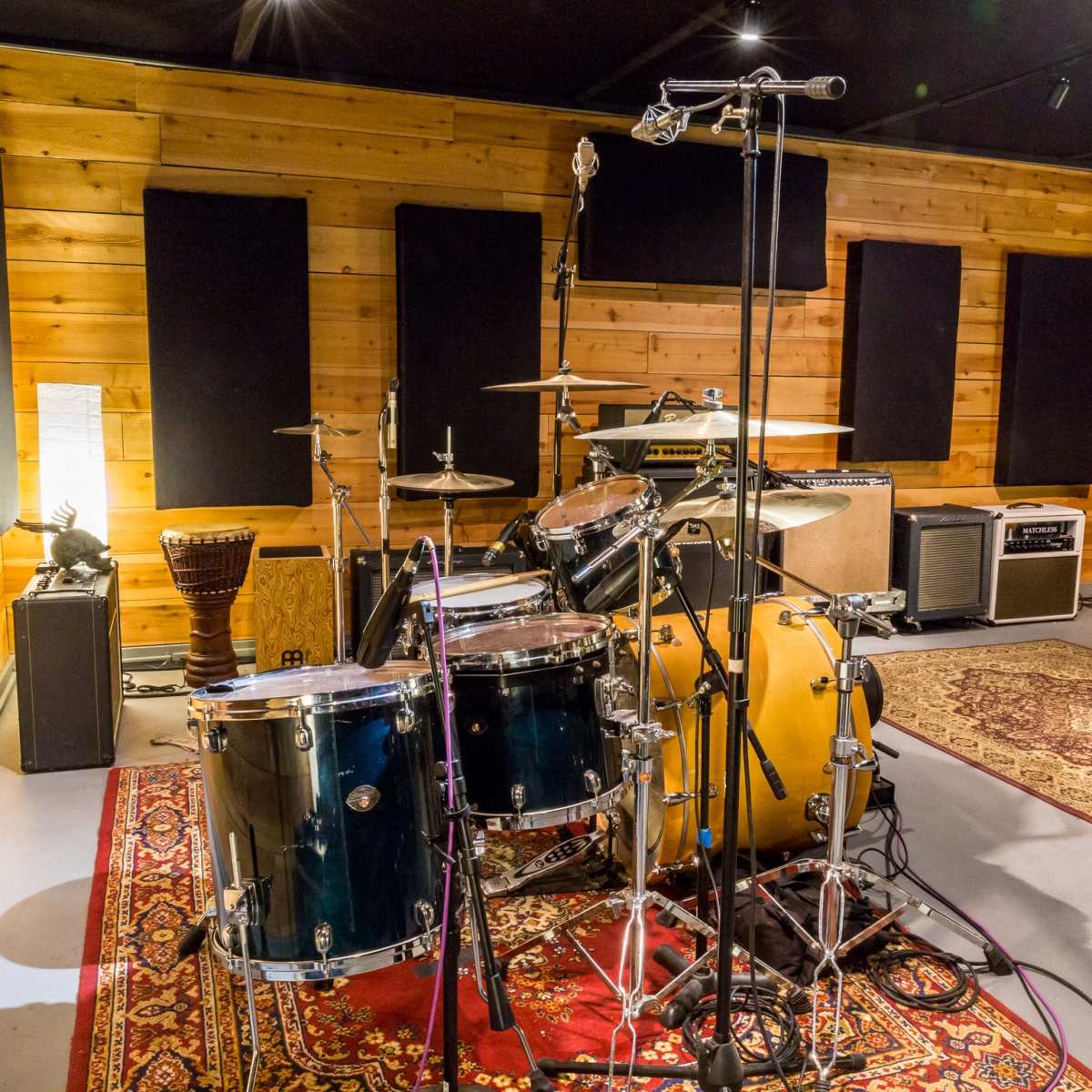 A drum set arranged in a recording studio with wooden walls, microphones, and various musical instruments in the background.