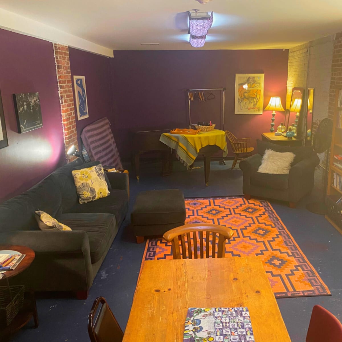 A cozy living space with purple walls, a wooden dining table, a dark sofa, and bookshelves filled with books.