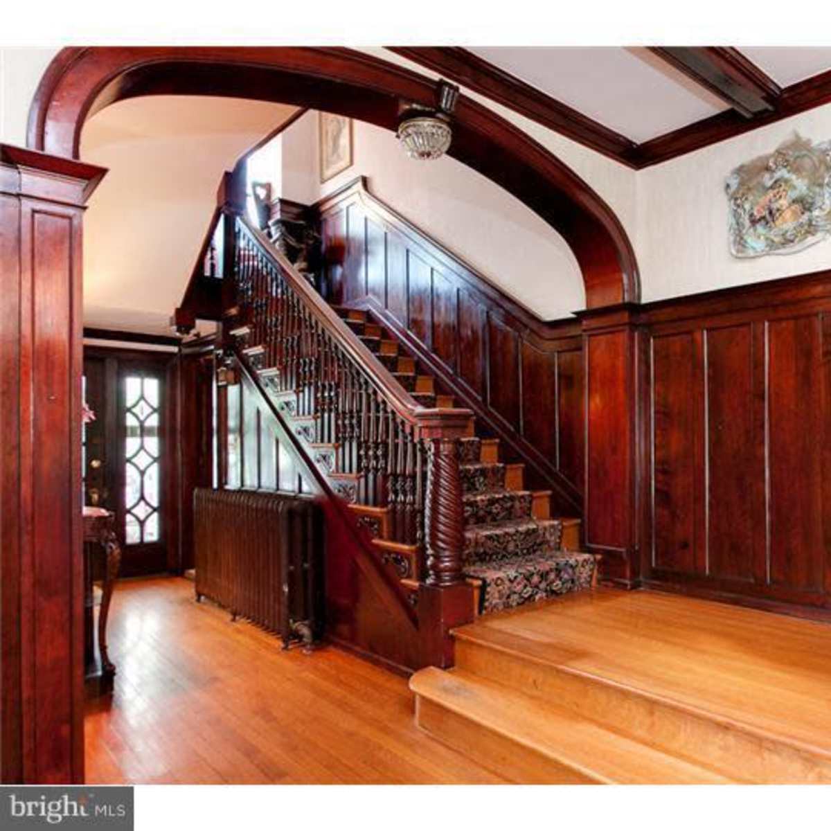 An interior entrance with a wooden staircase, dark wooden paneling, and a decorative railing.