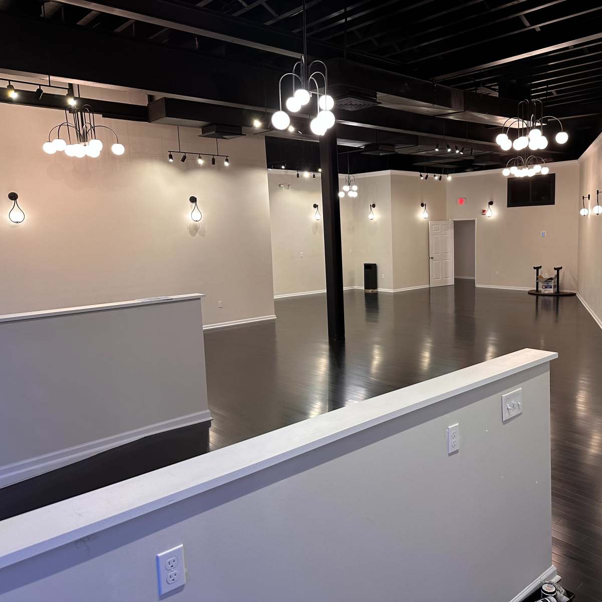 A spacious, empty interior with polished dark flooring and various hanging light fixtures on the walls and ceiling.
