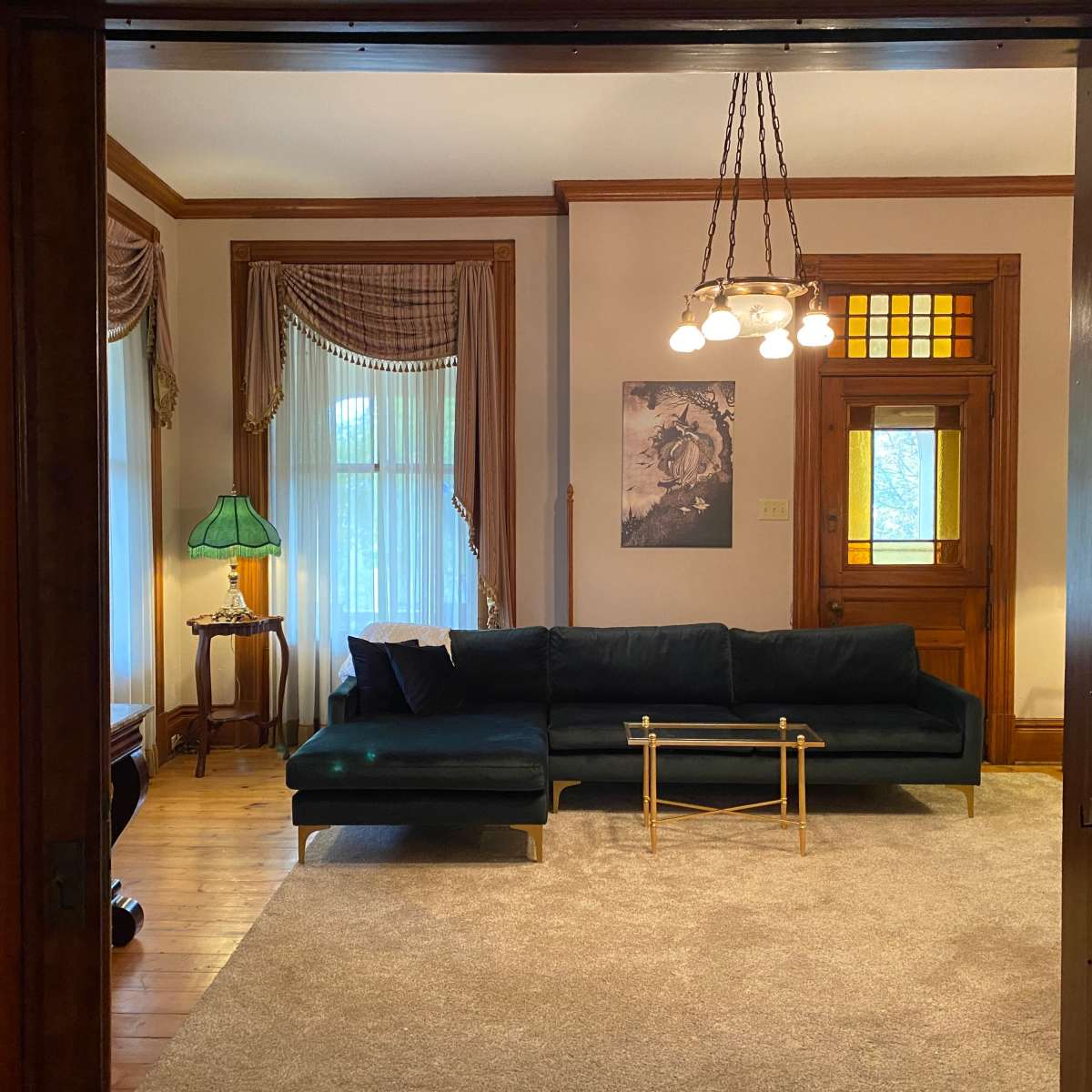 A dark blue sectional sofa faces a light-colored rug in a room with large windows, a lamp, and a wooden door.