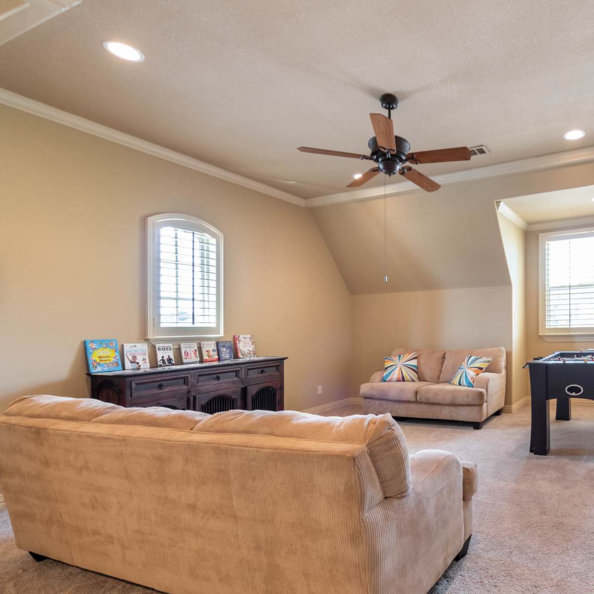 A spacious room with a ceiling fan, a seating area, a desk, and windows allowing natural light.