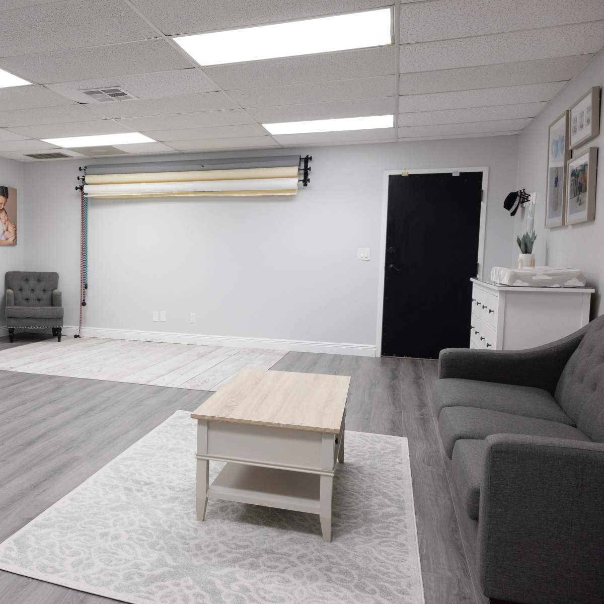 A spacious, well-lit room with gray walls, wood flooring, and various seating and display furniture, including a gray sofa and a coffee table.