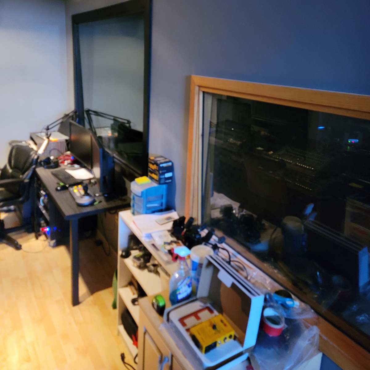 A small recording studio with a control desk, computer monitors, and various equipment neatly arranged on shelves.