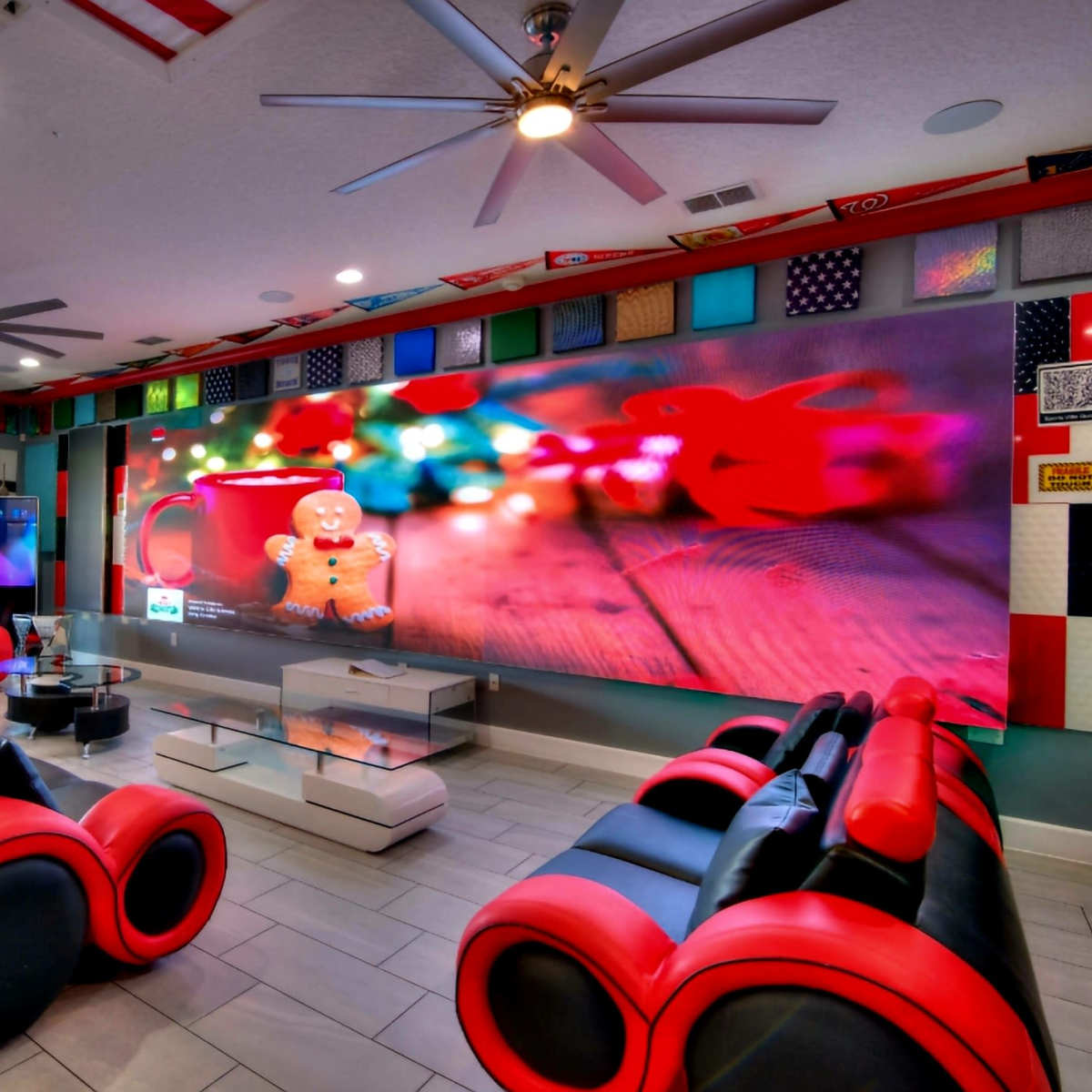 The room features a modern lounge area with red and black furniture, a large screen displaying colorful decor, and an extensive wall adorned with various flags.