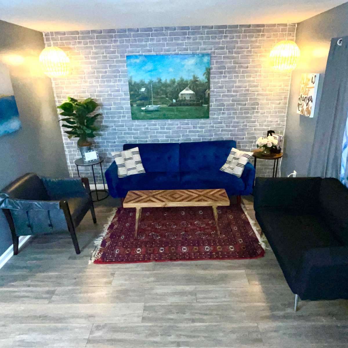 A cozy living room with a brick accent wall, two sofas facing each other, a wooden coffee table in the center, and decorative elements like plants and artwork.
