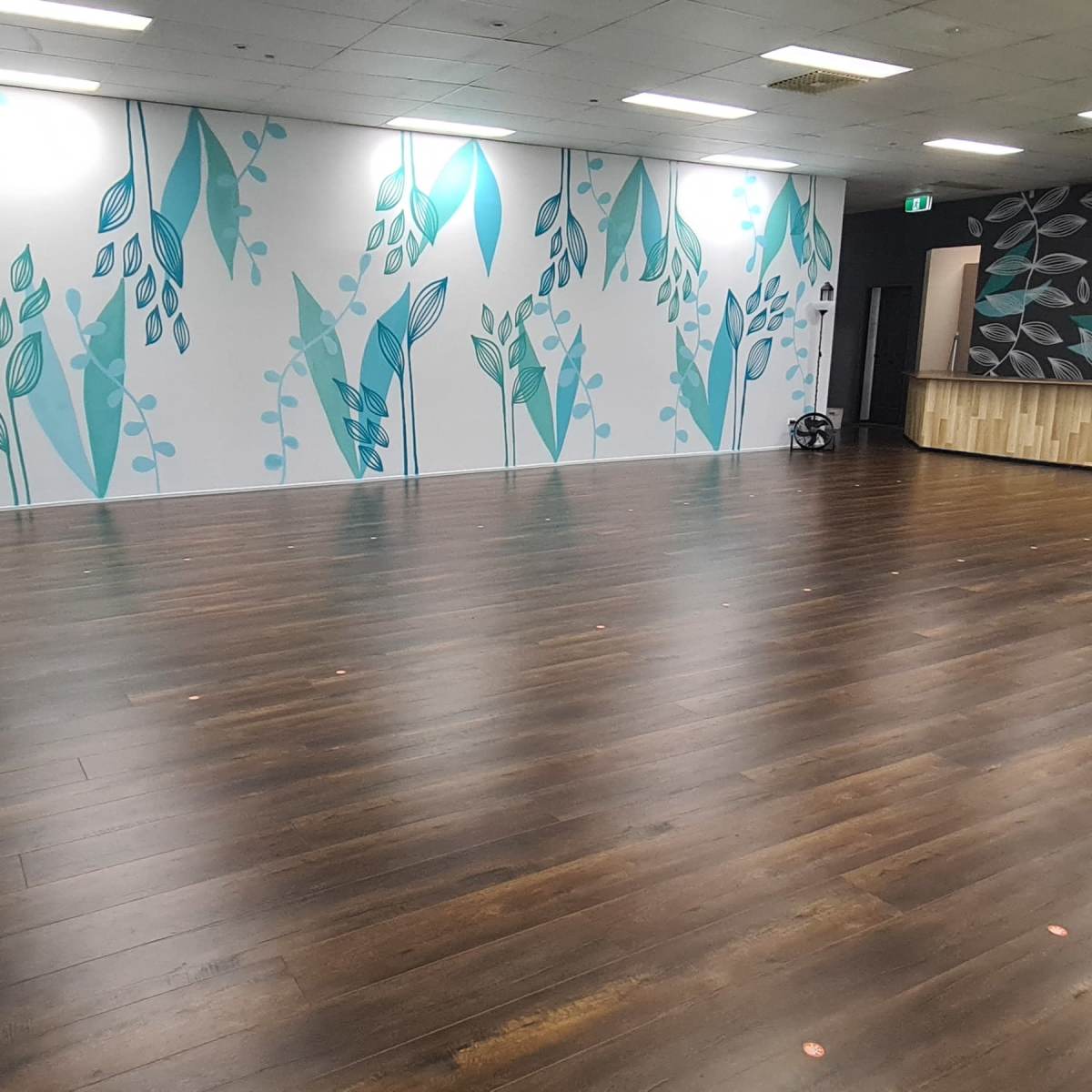 A spacious room with wooden flooring and walls decorated with blue and green leaf patterns.