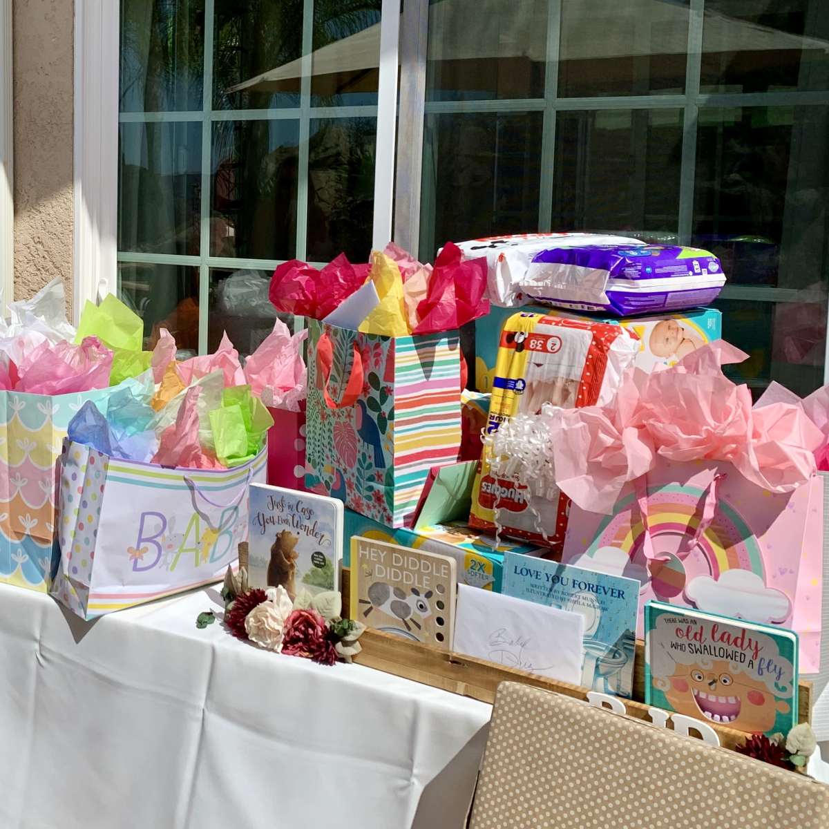 A table is adorned with colorful gift-wrapped boxes and bags, surrounded by tropical plants and a sunny outdoor setting.