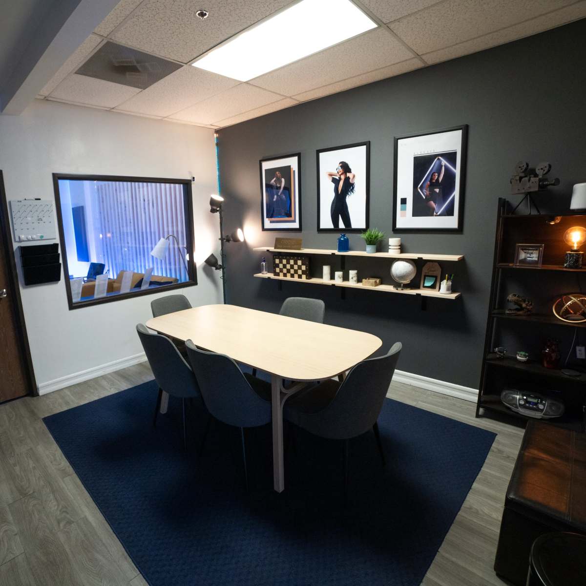 A modern conference room with a round table surrounded by chairs, framed photographs on the walls, and a shelf displaying decorative items.