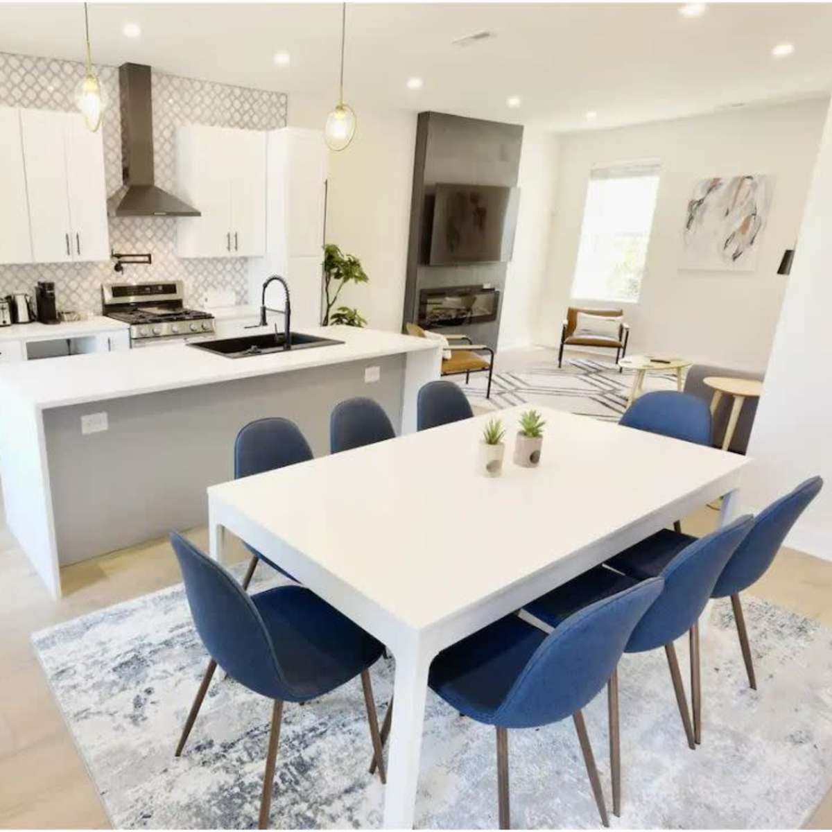 A modern kitchen and dining area with white cabinetry, a large island, and a table set for eight.