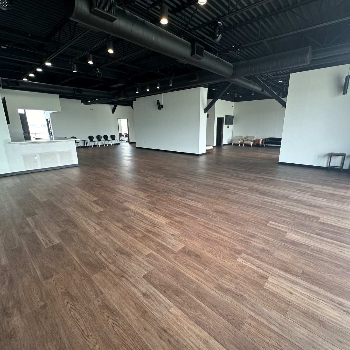An empty indoor space with wooden flooring and minimalist design, including a bar area and seating arrangements along the walls.