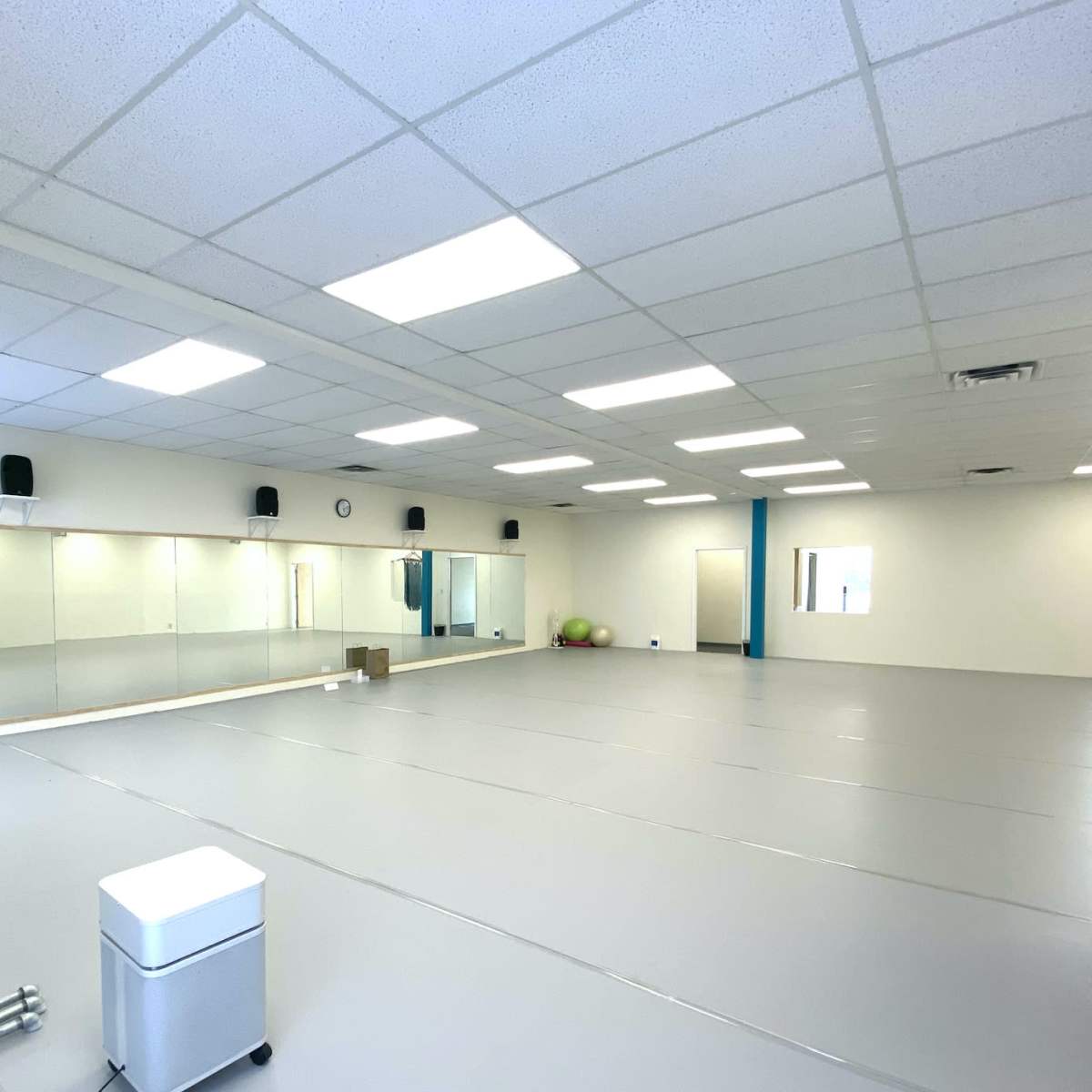 A spacious, empty room with mirrored walls, gray flooring, and minimal furnishings.