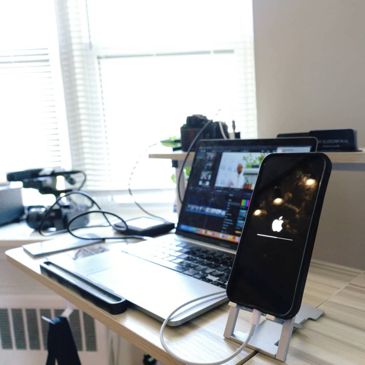 A smartphone with a loading screen is positioned on a stand next to a laptop on a desk.