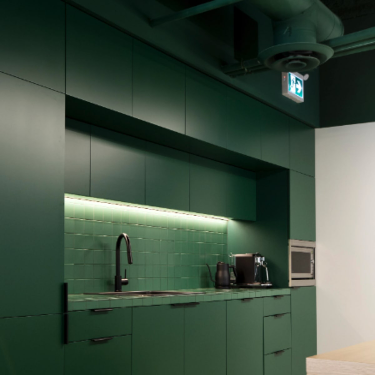 A modern kitchen with dark green cabinets, a backsplash of square tiles, and stainless steel appliances.