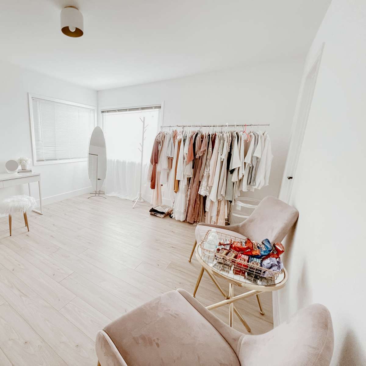 A tidy, minimalistic room features a clothing rack filled with garments, a makeup vanity, and two chairs.