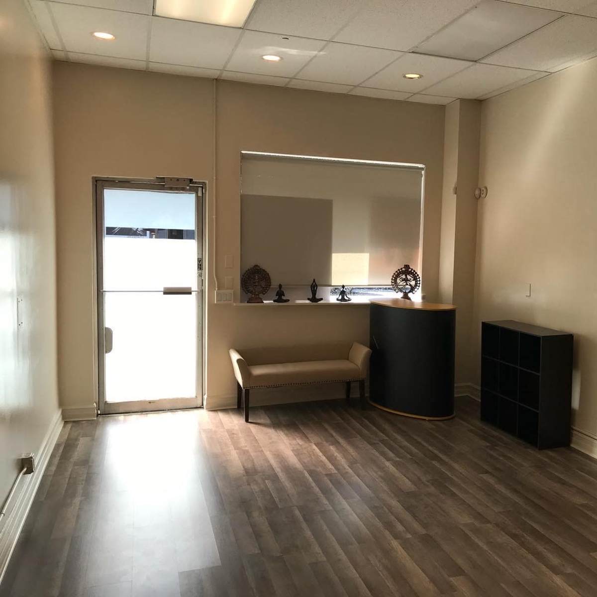 A sparsely furnished interior of a shop or office with light-colored walls, a bench, and a small display area near the entrance.