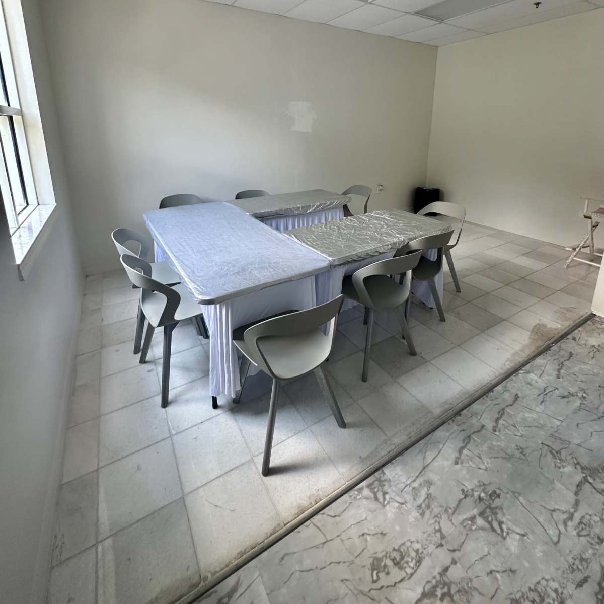 A spacious, empty meeting room features a long table covered with a tablecloth and surrounded by several chairs.