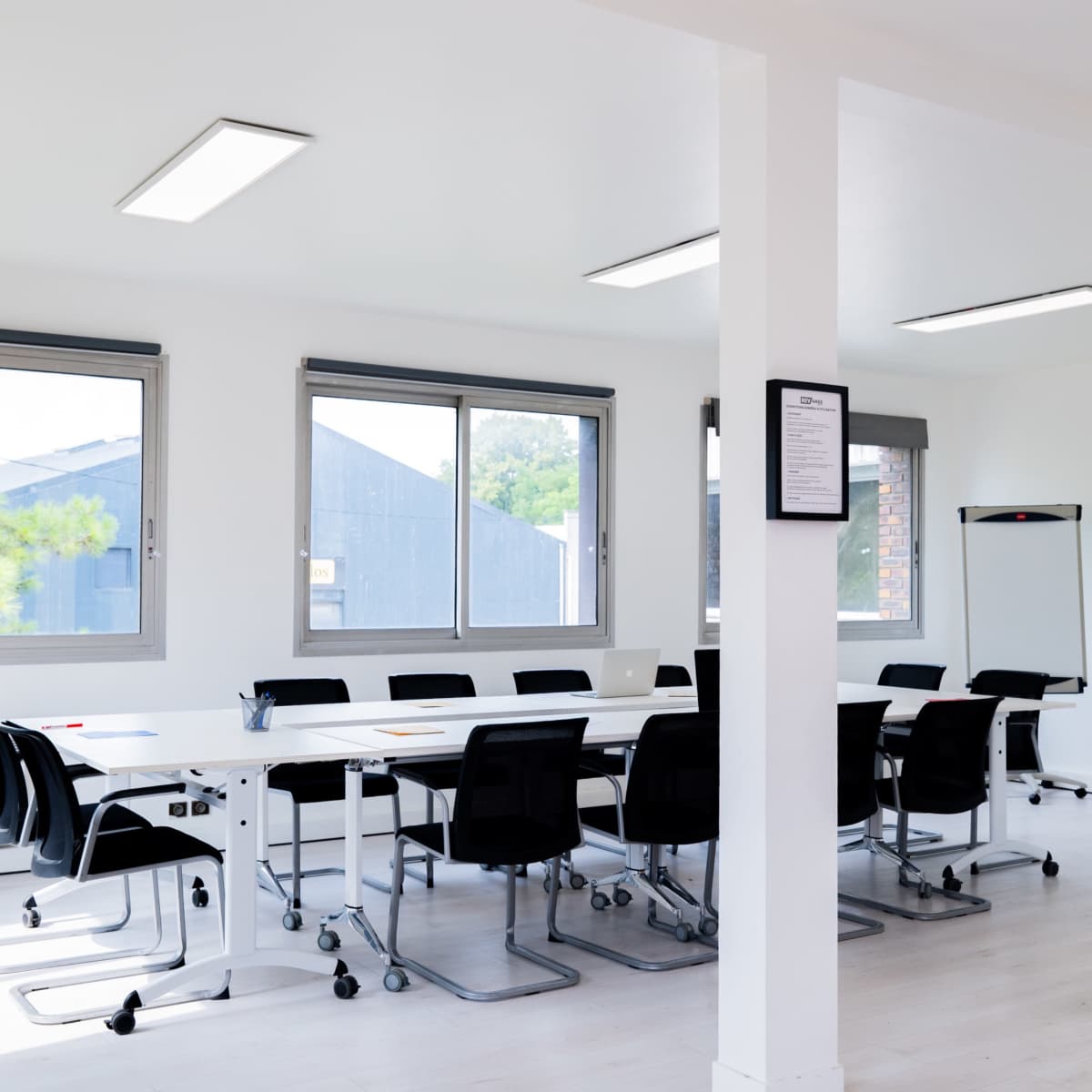 A bright meeting room furnished with a long table surrounded by black chairs, a whiteboard, and a yellow armchair.