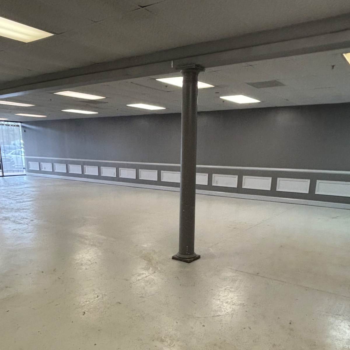 An empty room with a gray wall, a column in the center, and a large window at one end.