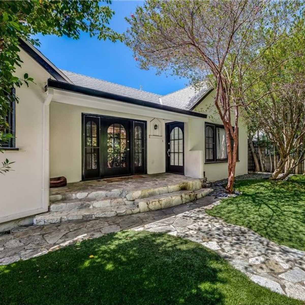 A stone pathway leads to the entrance of a house with a landscaped yard and surrounding trees.