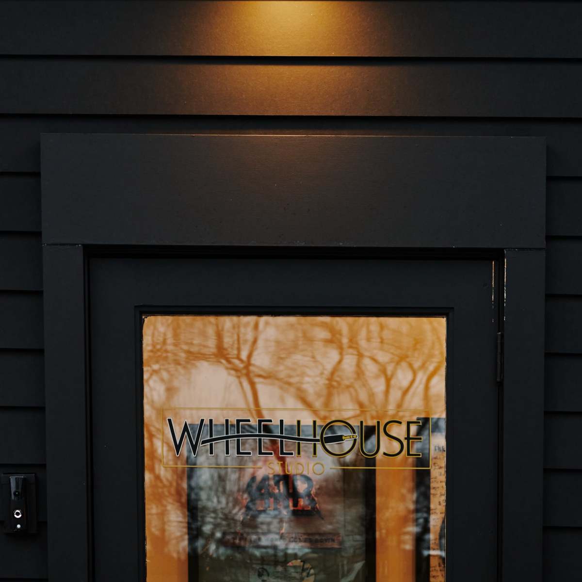 A black building features a well-lit entrance with a door displaying the word "WHEELHOUSE" along with an illuminated exterior light.