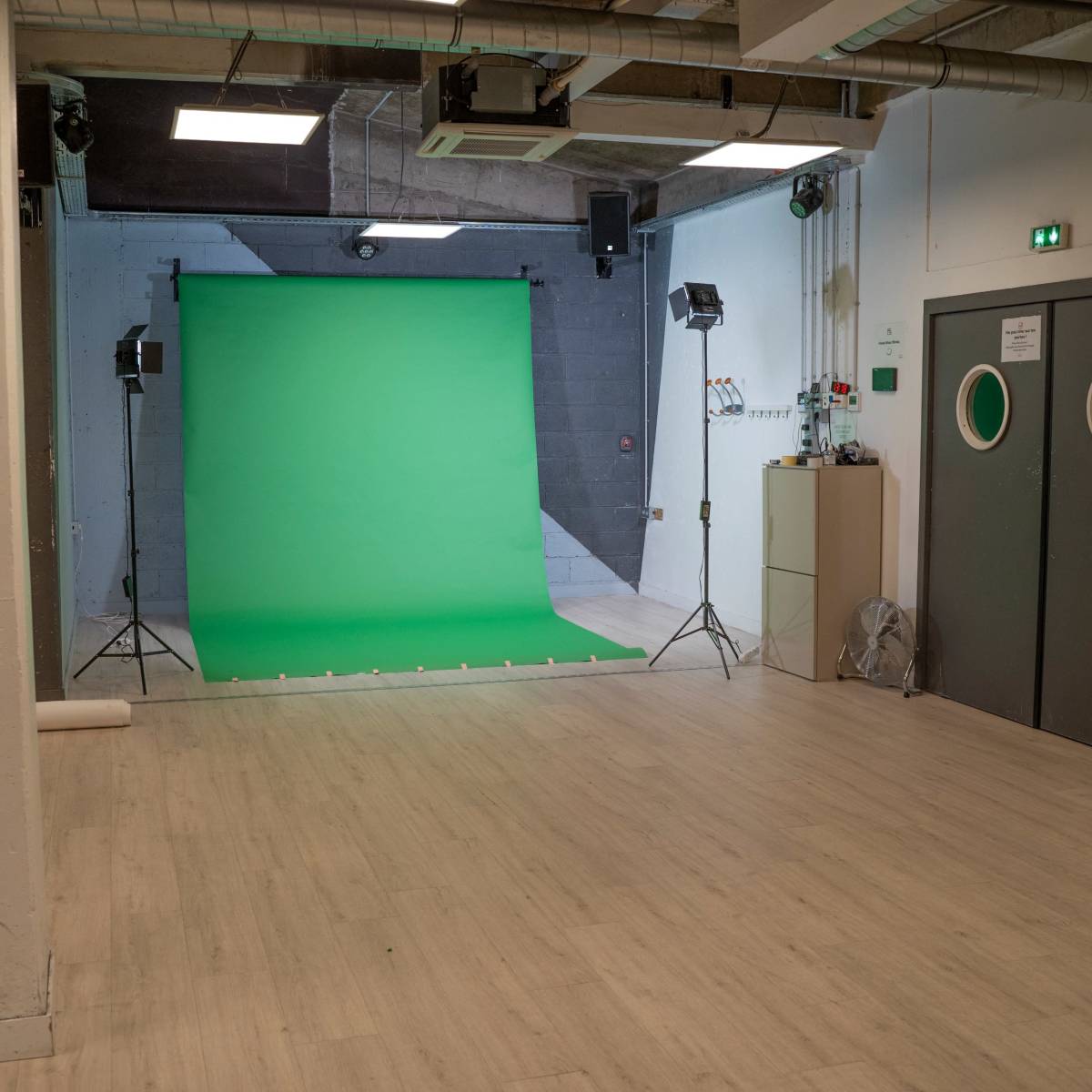 A studio space with a green backdrop and two lights set up for photography or video production.