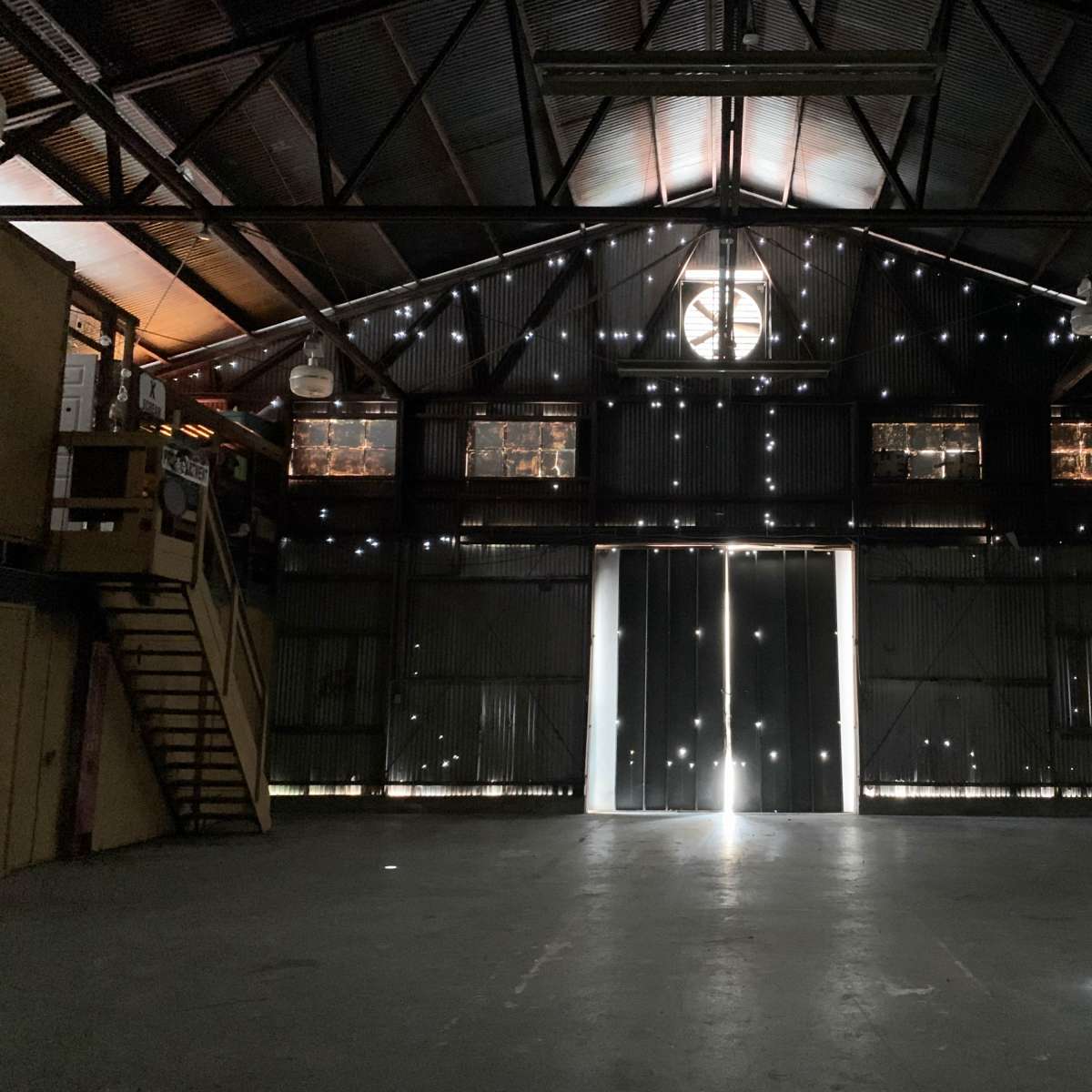 An empty warehouse features large doors at the back, with light streaming in through gaps in the walls and ceiling.