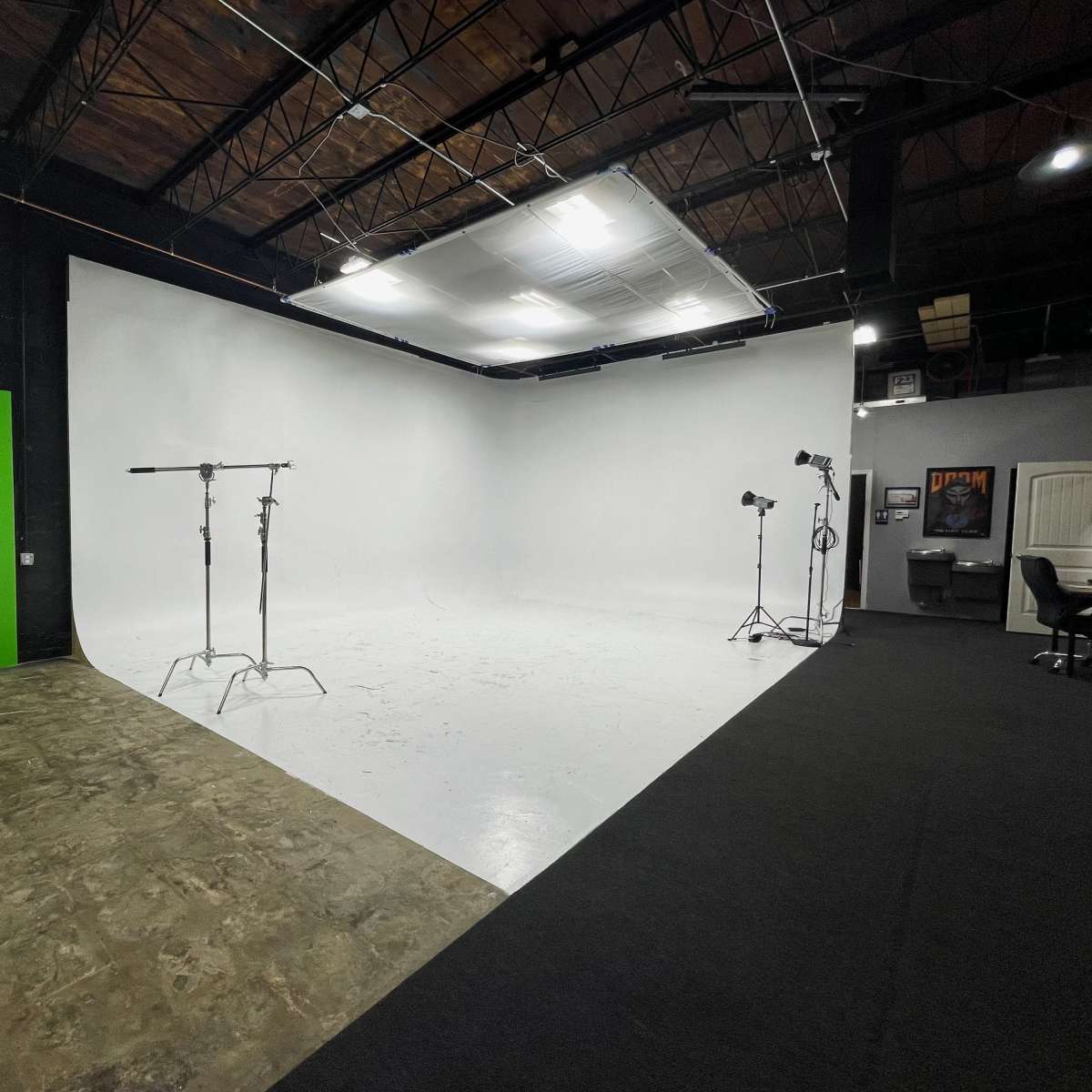 A photography studio with a white backdrop, a green screen, and lighting equipment set on stands.